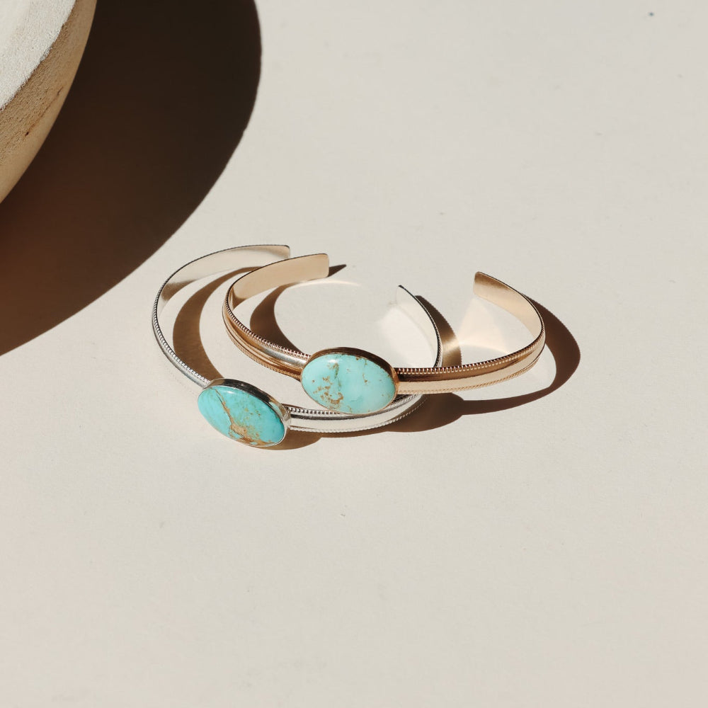 14k Gold Fill and Sterling Silver bezel set turquoise cuff on a smooth thick band with textured edges photographed on a beige background in the sunlight