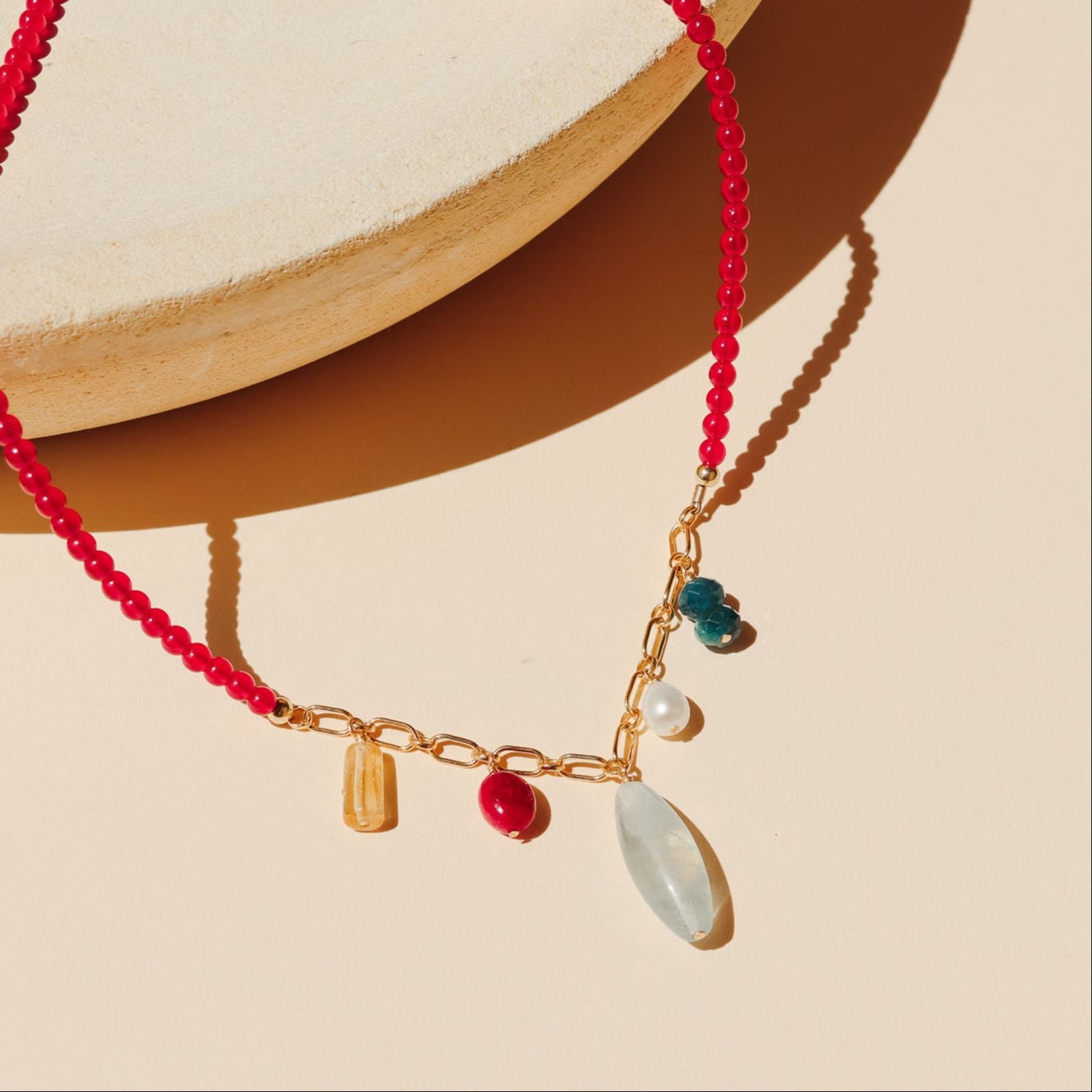 necklace with ruby beads and gold chain with gemstone charms on a light dish