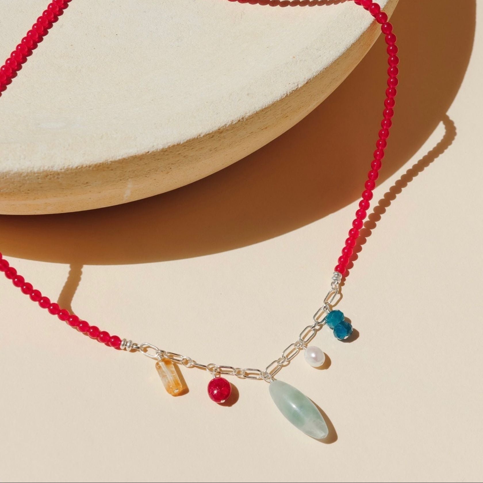 necklace with ruby beads and silver chain with gemstone charms on a light dish