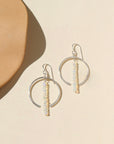 A sterling silver hoop featuring white opal gemstones dropped 2" from earring post. Earrings are displayed on a cream back drop in the sunlight. 