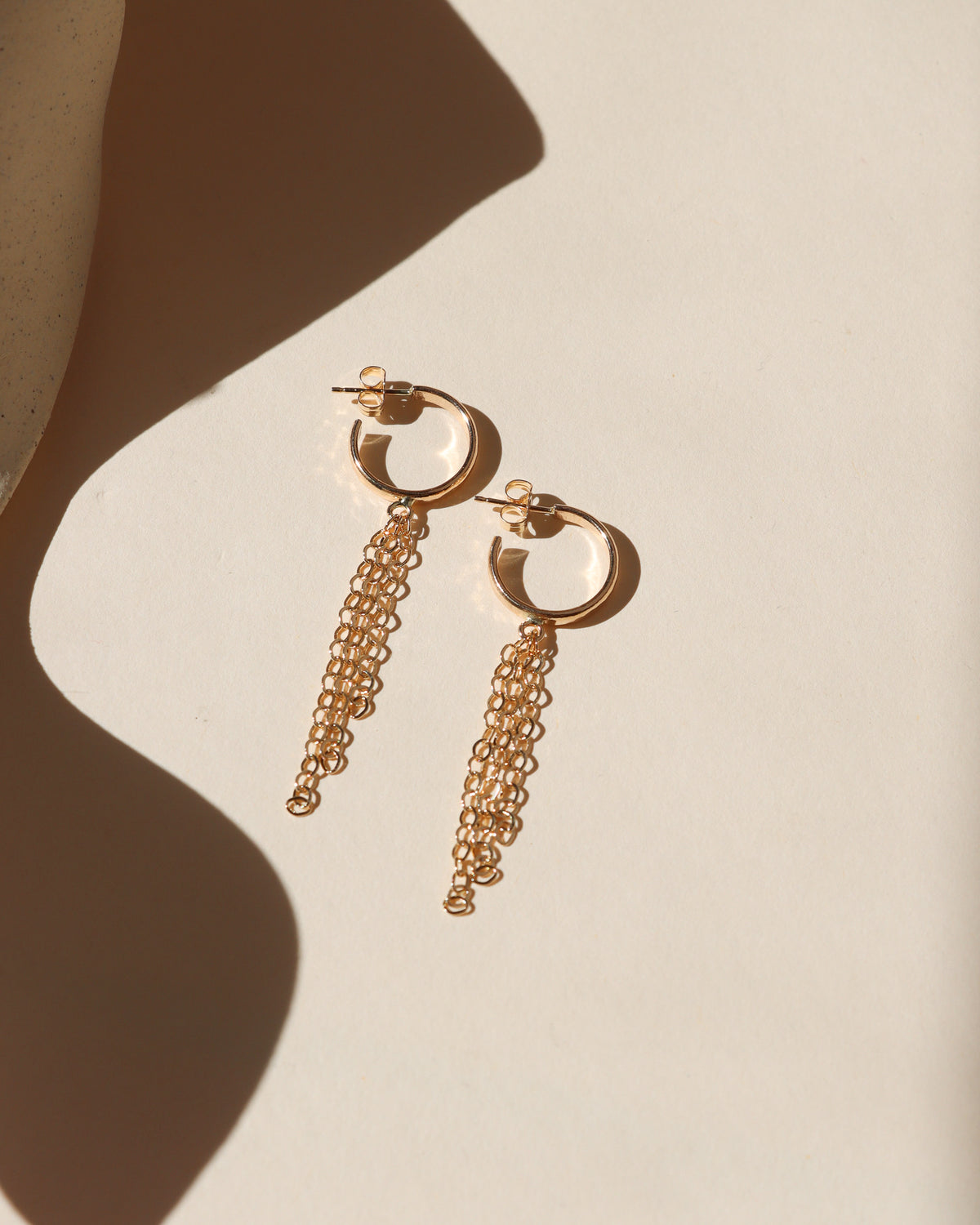 Delicate hoop earrings with cascading chain fringe, shown in warm gold fill and bright silver finishes.