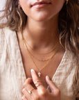 a mother of pearl white cross pendant on a 14k gold fill chain, photographed on a model wearing a cream linen vest and other 14k gold fill chain necklaces made by Token Jewelry