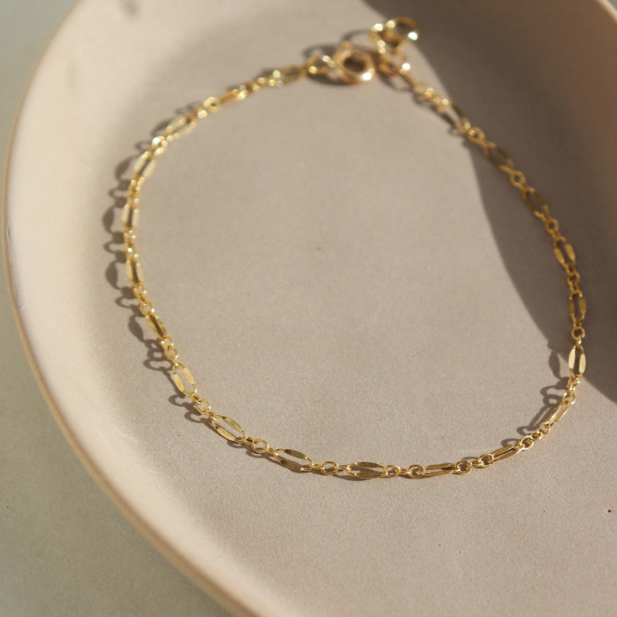 14k gold fill Sylvie bracelet laid on a tan plate in the sunlight.