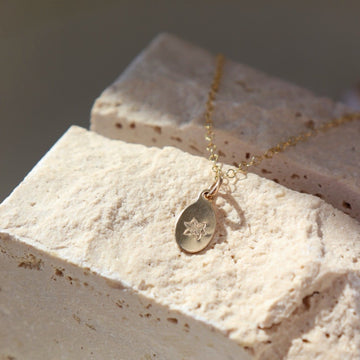 14k gold fill Birth Flower Necklace. Necklace laid across a cream stone. Handmade in Eau Claire Wisconsin. 