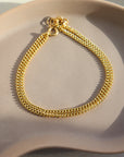 14k gold fill La Mer bracelet laid on a tan plate in the sunlight.