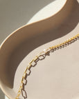 14k gold fill bracelet place on top of a peach colored plate. Sitting in the sunlight, featuring the narrow link chain, a tiny pearl gemstone, and the Dylan chain. The jewelry is handmade in Eau Claire Wisconsin, at Token Jewelry.