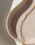 14k gold fill bracelet place on top of a peach colored plate. Sitting in the sunlight, featuring the narrow link chain, a tiny pearl gemstone, and the Dylan chain. The jewelry is handmade in Eau Claire Wisconsin, at Token Jewelry.