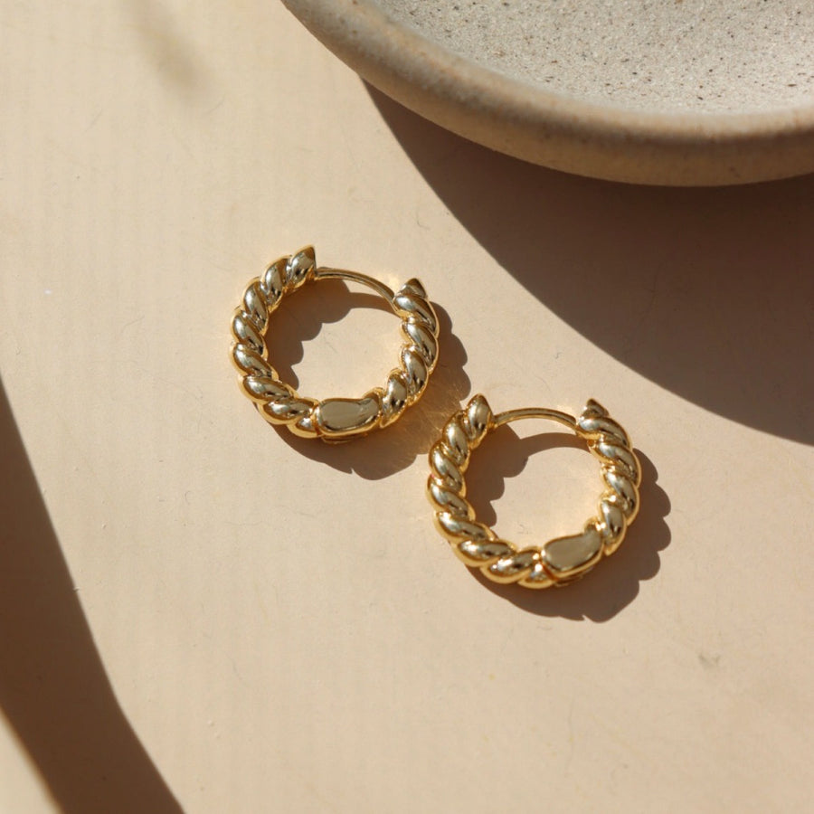 14k gold fill Croissant Huggie Hoops laid on the peach paper.