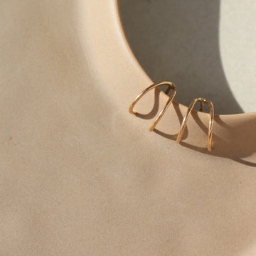 14k gold fill wishbone studs laid on a tan plate in the sunlight.