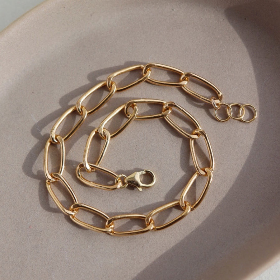 14k gold fill Curve Bracelet sitting on the peach colored plate. Handmade in Eau Claire Wisconsin. 