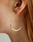 Model wearing Hammered Paloma Hoops. These earrings feature a wire around 1/2 inch shaped like an oval, then followed by the other half of the oval that is hammered.