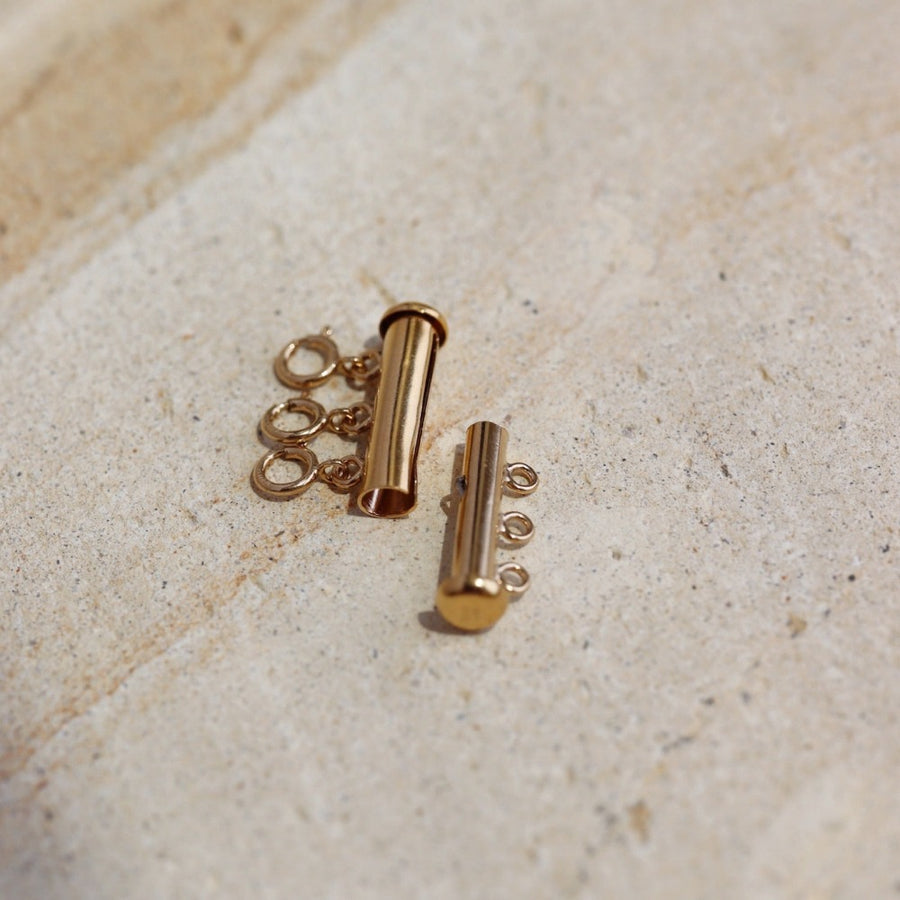 14k gold fill Necklace layering clasp laid on a stone plate in the sunlight. 