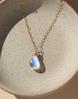 14k gold fill necklace with natural teardrop moonstone full of blue flash laid on a gray moonstone plate.