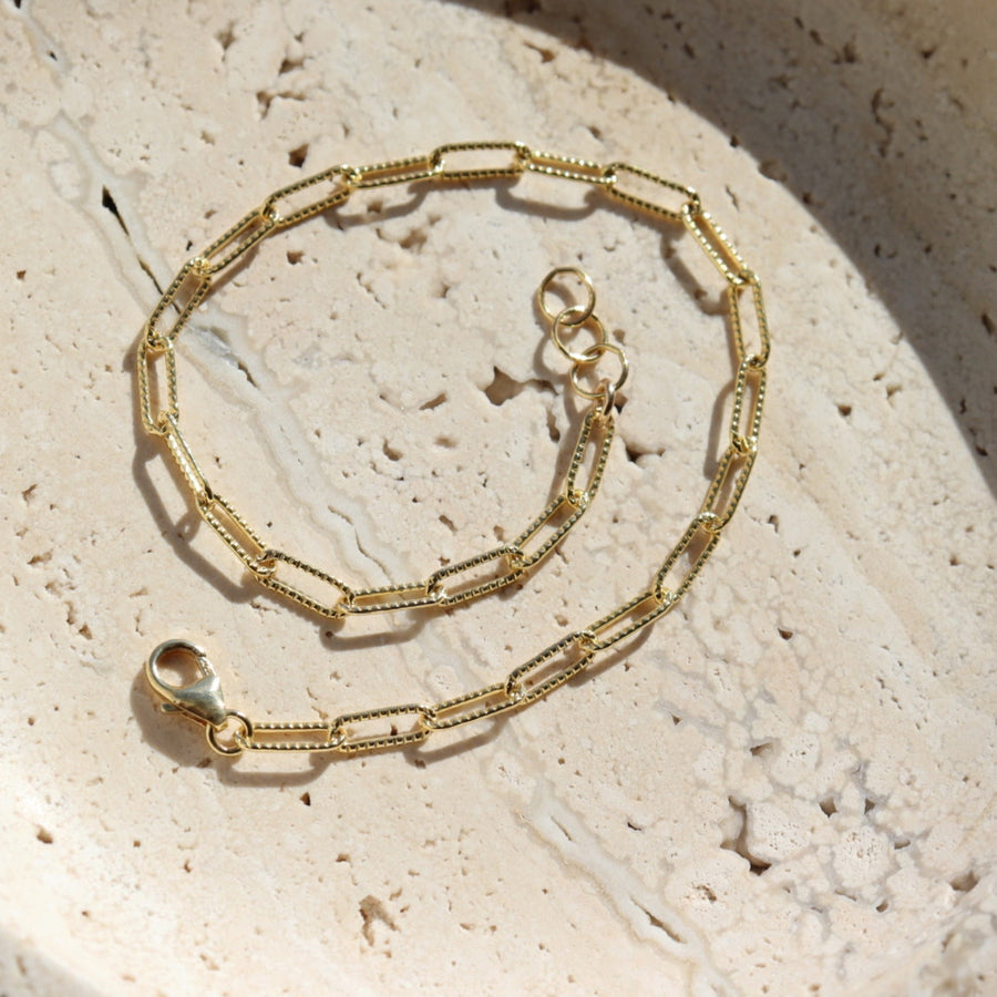 14k gold fill piper bracelet set on a tan stone plate in the sunlight.