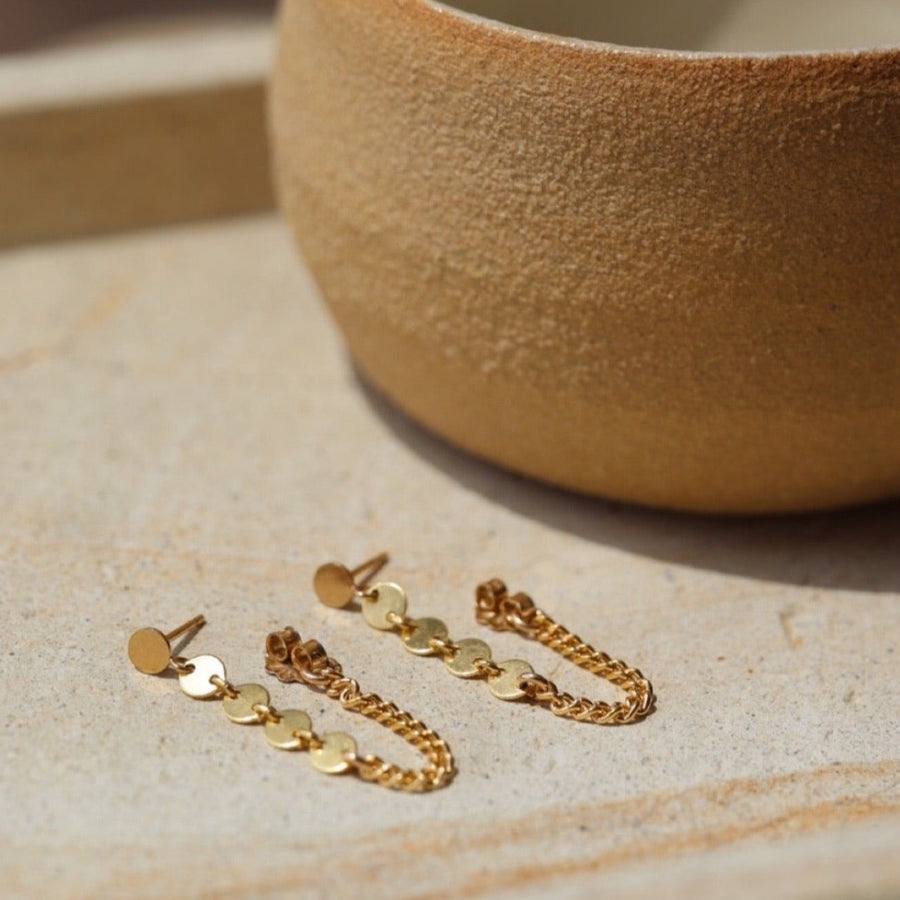 14k gold fill Starlight chain studs laid on a tan plate in the sunlight. This earring features the polka dot stud with a dangle of the starlight chain along with the la mer chain. Making this the perfect every day earring.