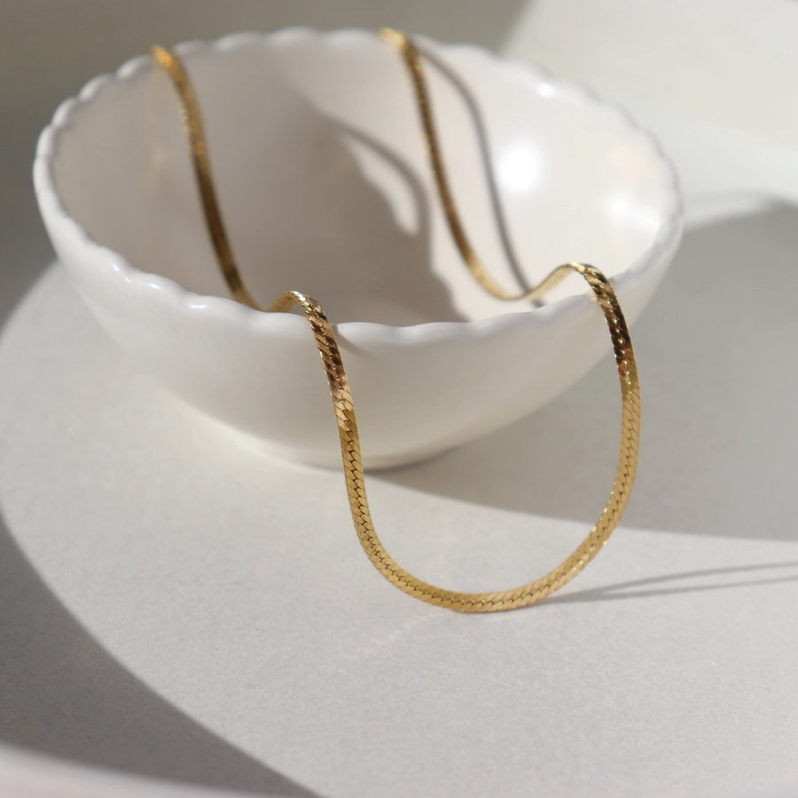 14k gold fill Luxe Herringbone Chain on a white bowl in the sunlight.